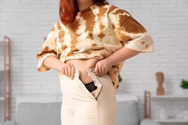 Image of woman trying to do her trousers up after pregnancy weight gain Eccles