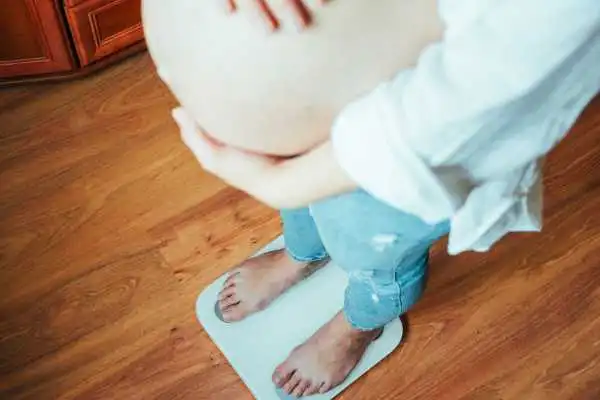 Image of woman weighing herself and experiencing weight gain through pregnancy Eccles